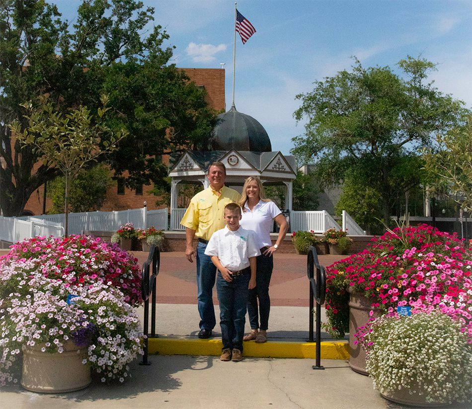 Family posing in front of flower beds.